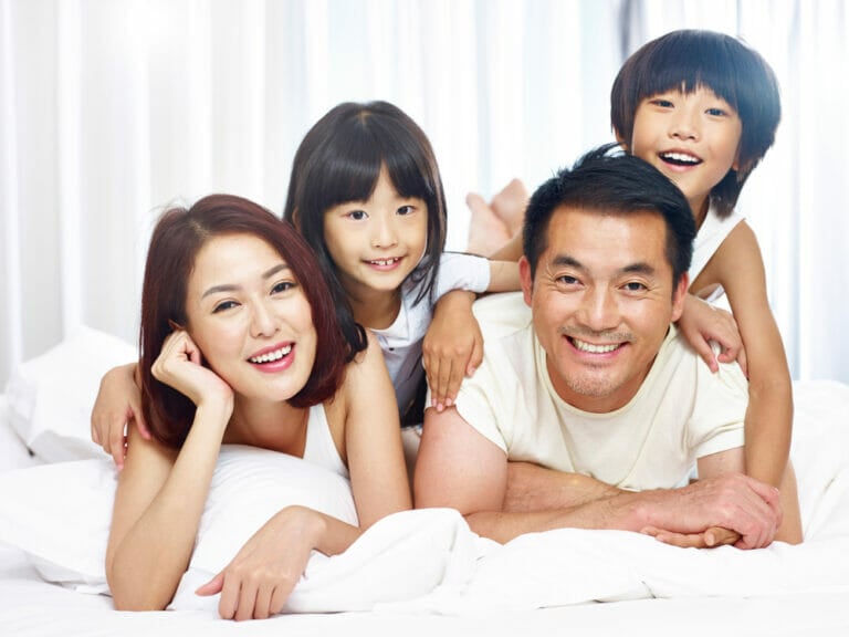 A family of four smiling while lying together on a white bed