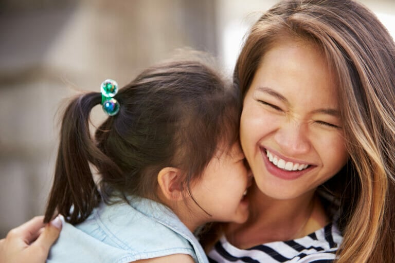 A young girl hugs a smiling woman outdoors