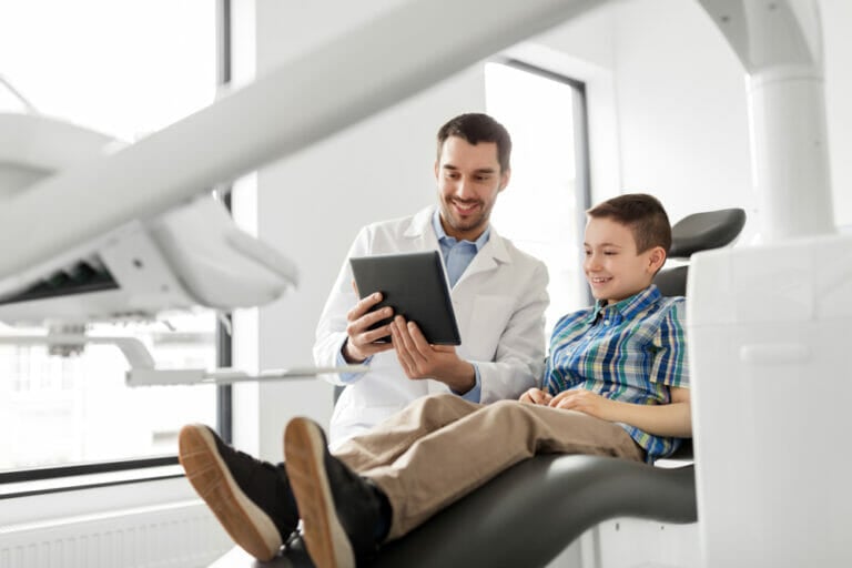 A dentist showing a tablet to a young boy sitting in a dental chair